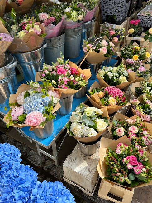 A vibrant display of freshly prepared floral bouquets arranged in metal buckets and wrapped in brown kraft paper, featuring a variety of flowers such as pink roses, white lisianthus, blue hydrangeas,